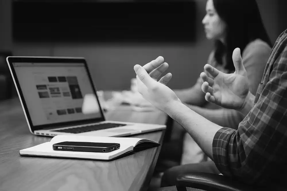 Mensen aan tafel met een laptop, in gesprek met handgebaren.